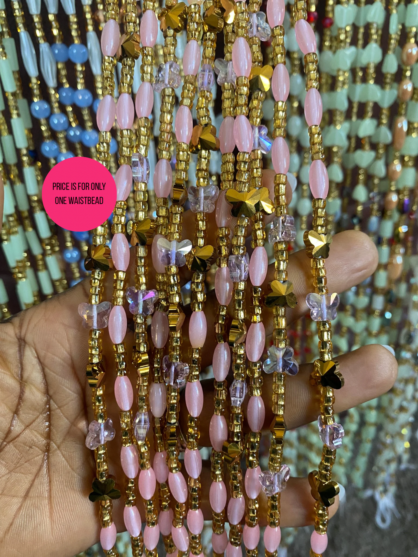 Close-up of a hand holding waistbeads of pink and gold beads with a blurred background.