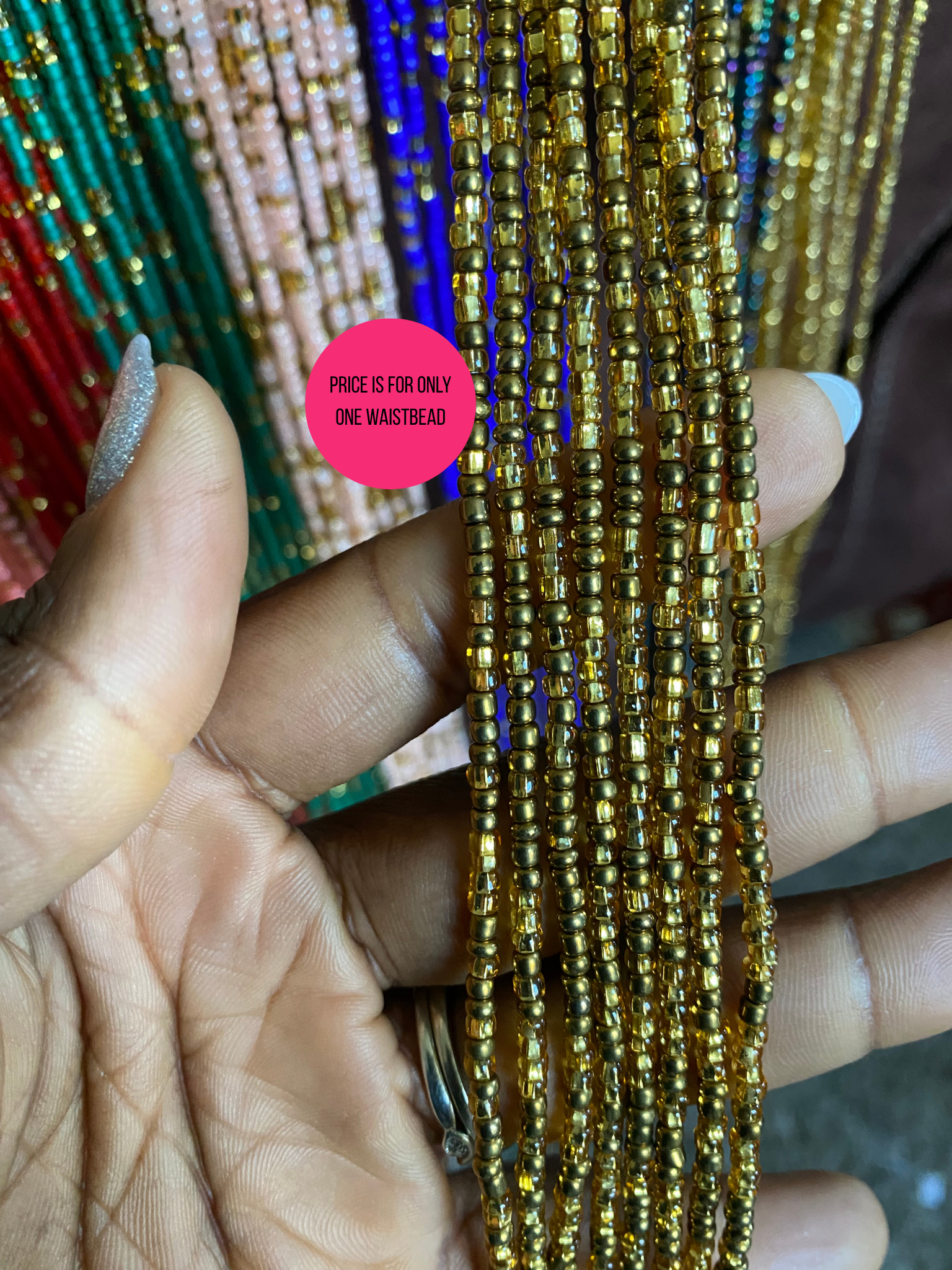 Gold beaded Waist Bead held between fingers with a pink label in the background