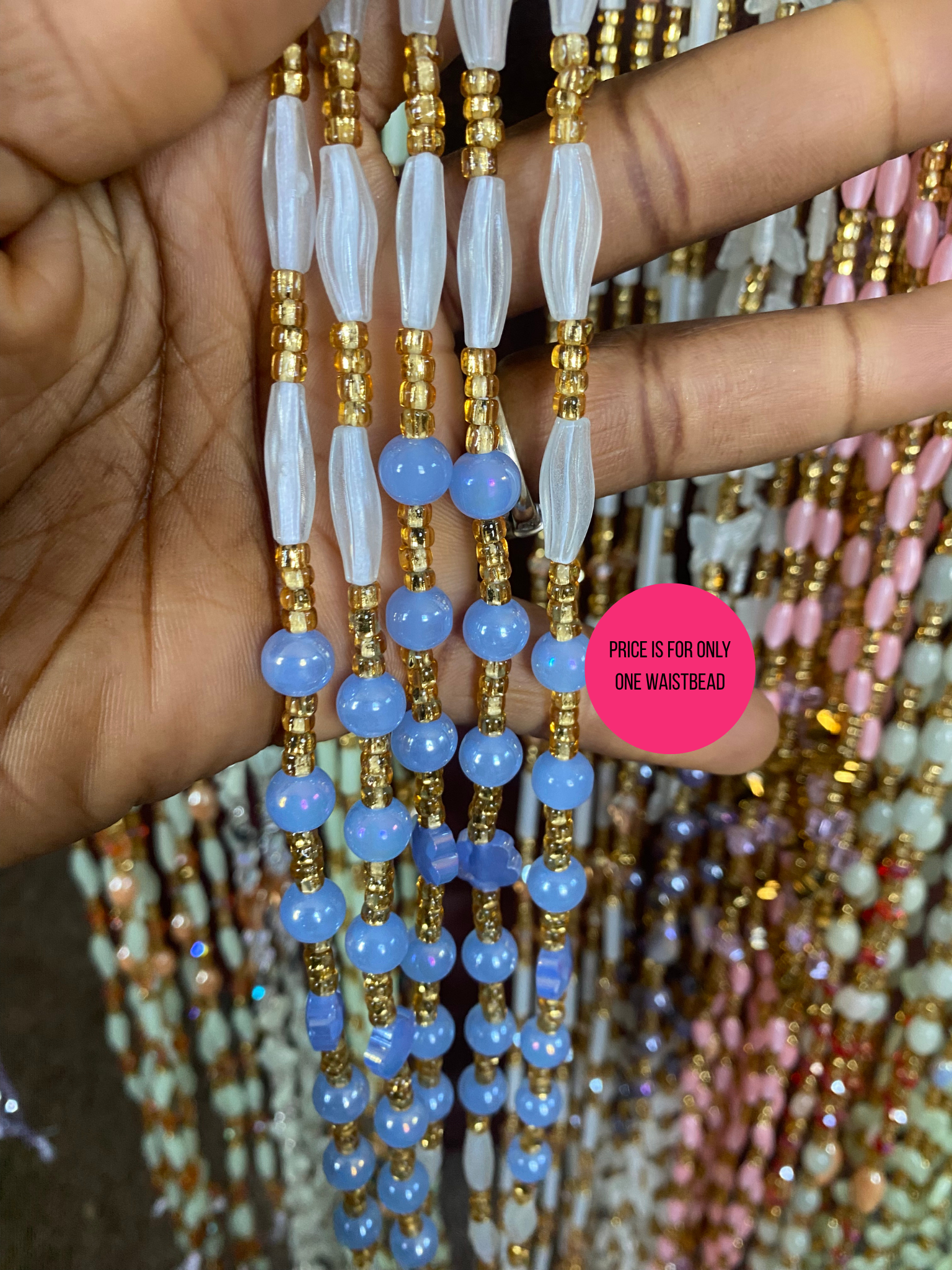 Close-up of a hand holding a Beaded Subtle Glow in the dark waist beads with blue beads and gold accents, surrounded by other colorful bead necklaces.