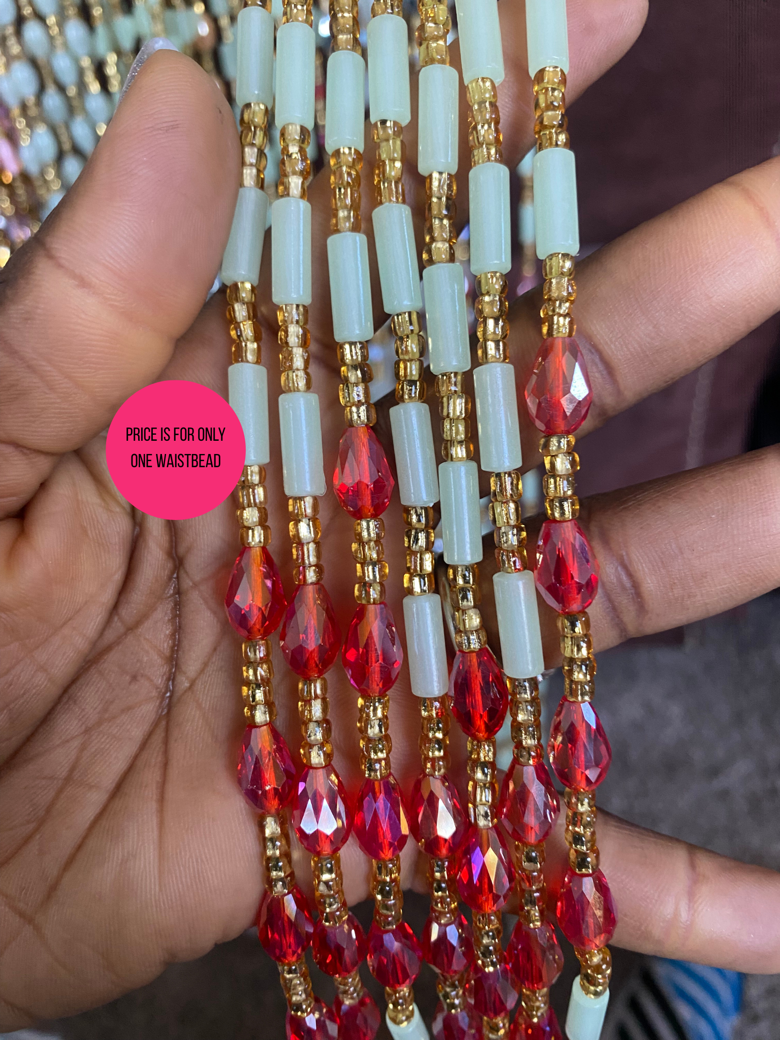 Beaded Subtle Glow in the dark waist beads with red, gold, and light blue beads held by a hand.