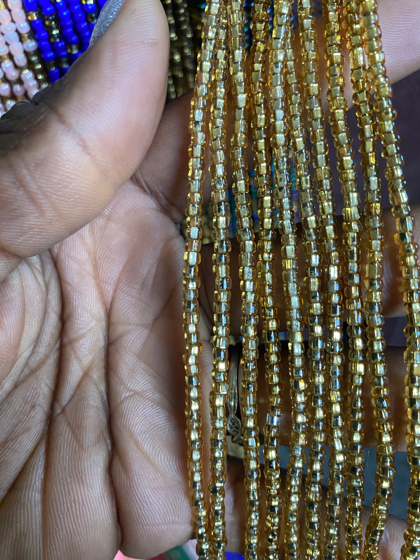 Close-up of a hand holding  strands of gold waist beads beads.