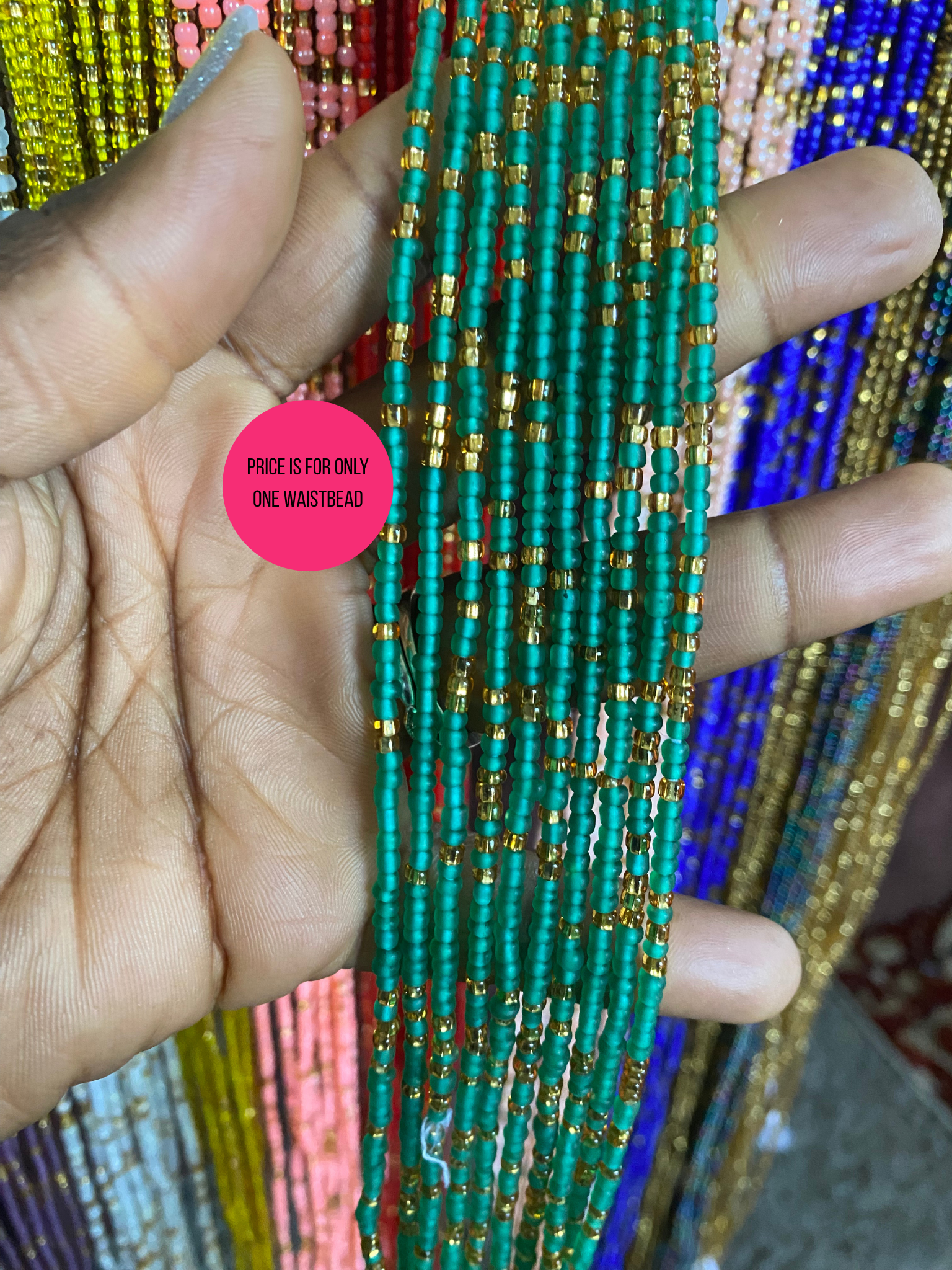 Hand holding a bundle of green beaded Waist beads strands with a pink label in the corner.