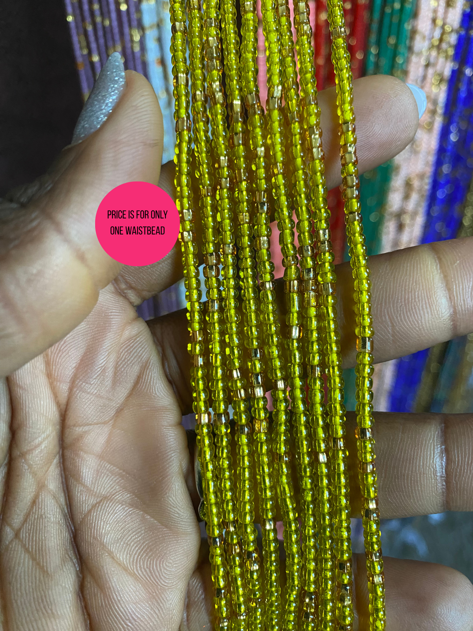 Close-up of a hand holding waistbeads  of yellow beads with a pink label.