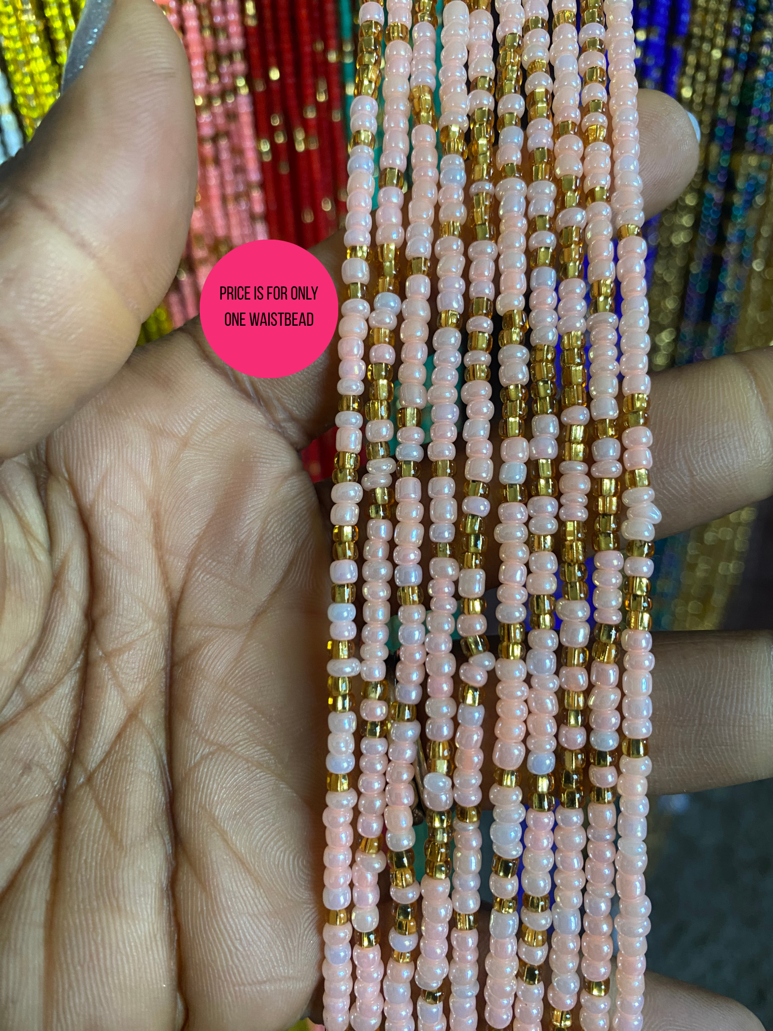 Close-up of a hand holding a beaded waist beads with pink and gold beads.
