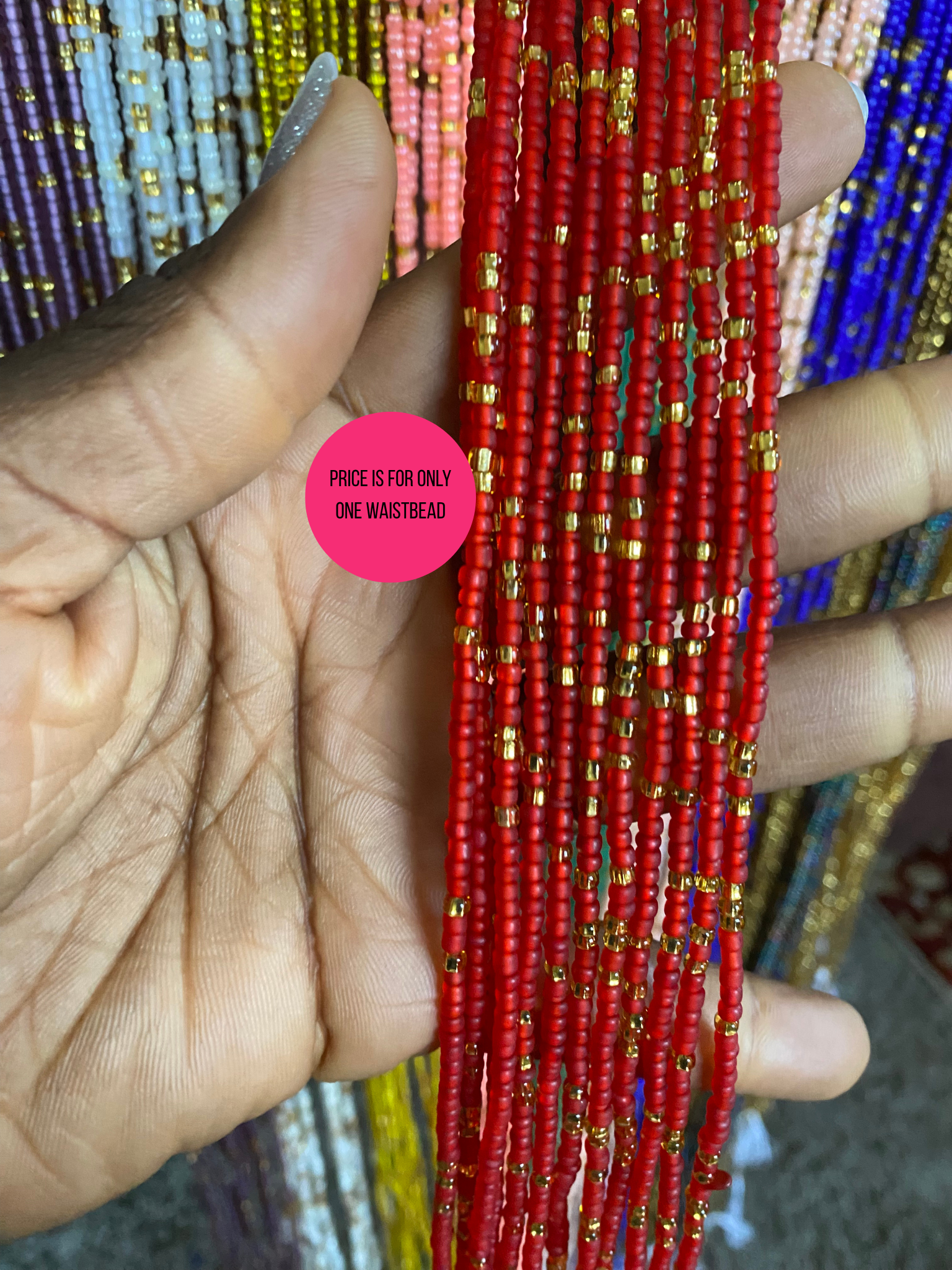 Red beaded waist bead  held between fingers with a pink label indicating price.