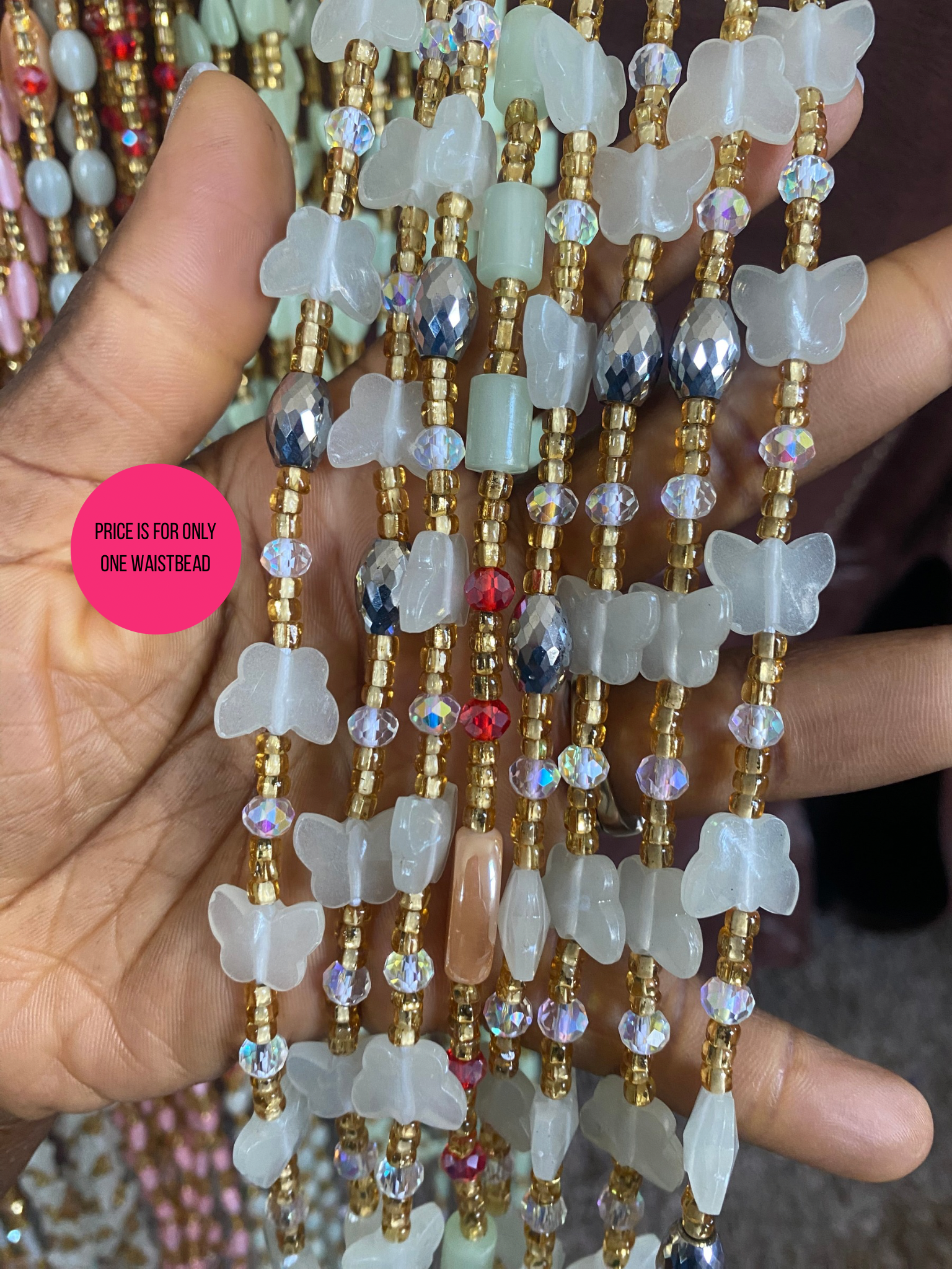 Butterfly-shaped waistbeads held by a hand with a pink label.