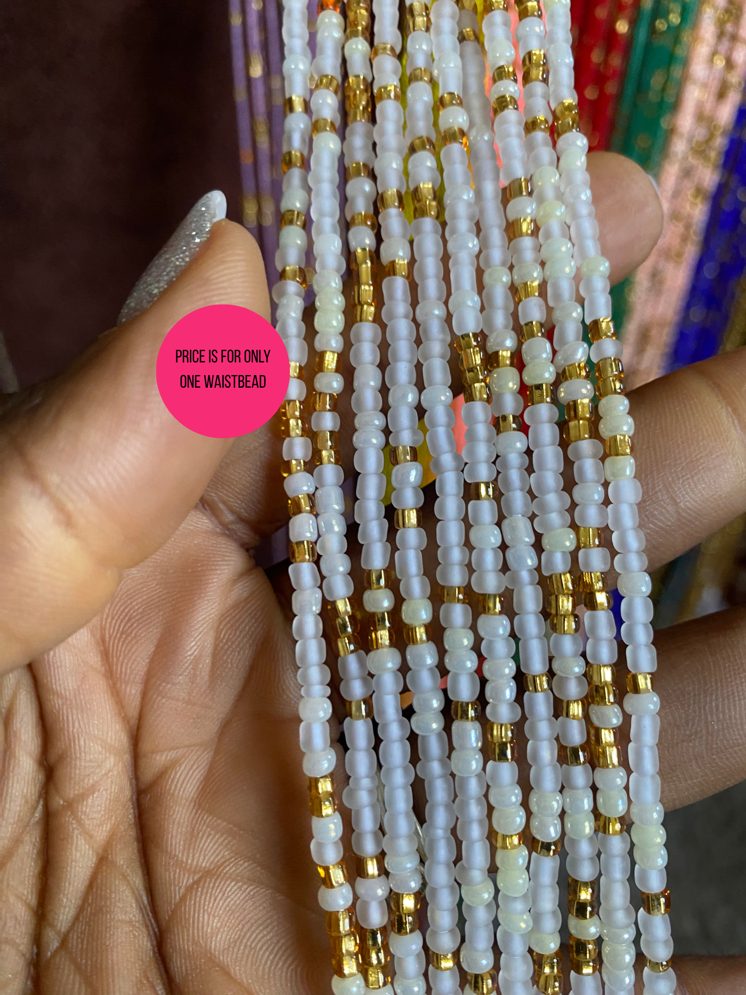 Close-up of a hand holding a bunch of waistbeads of white and gold 
