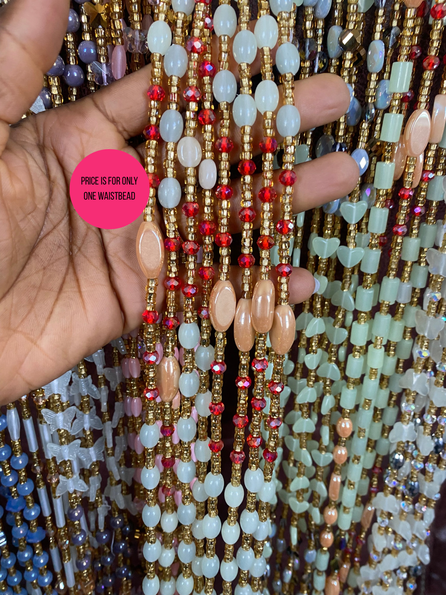 Hand holding a stack of colorful beaded waistbeads with a pink price tag label.